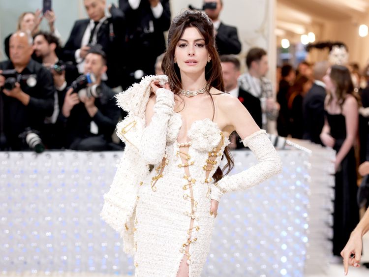 Anne Hathaway em um vestido Versace de tweed creme com detalhes dourados e sapatos plataforma creme