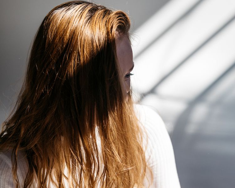 Uma mulher com cabelos castanhos acima do olho em pé na sombra