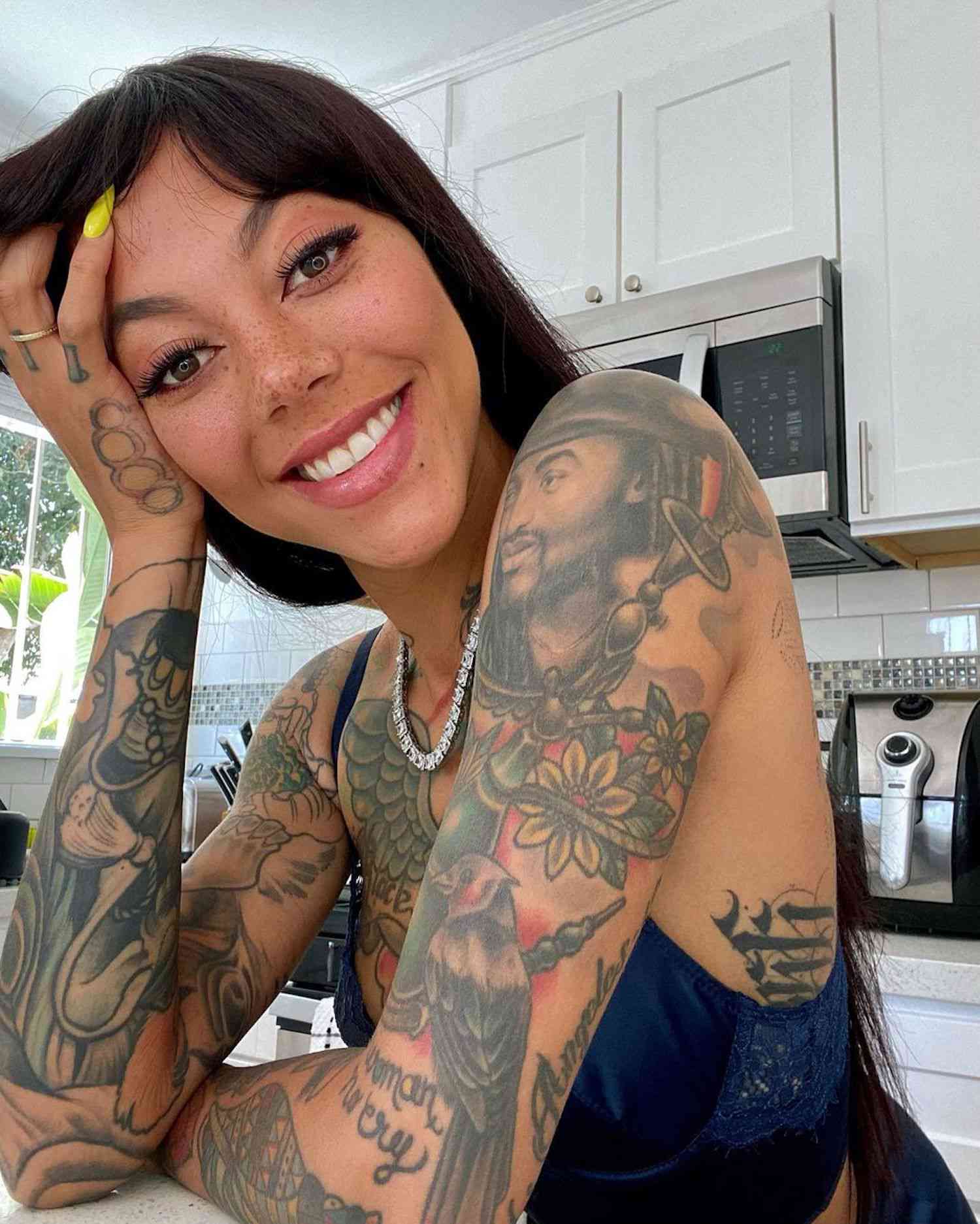 Foto de uma mulher com a cabeça apoiada na mão e muitas tatuagens nos braços e ombros