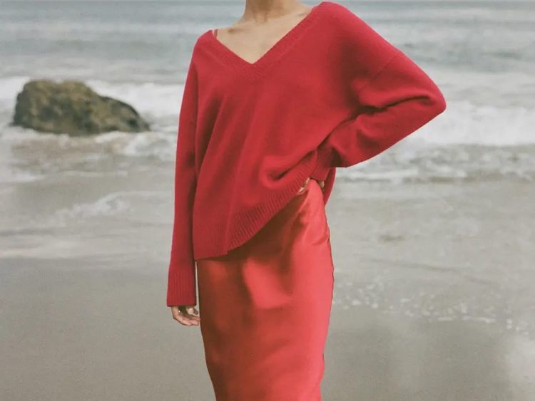 Mulher vestindo um suéter vermelho sobre um vestido de seda na praia