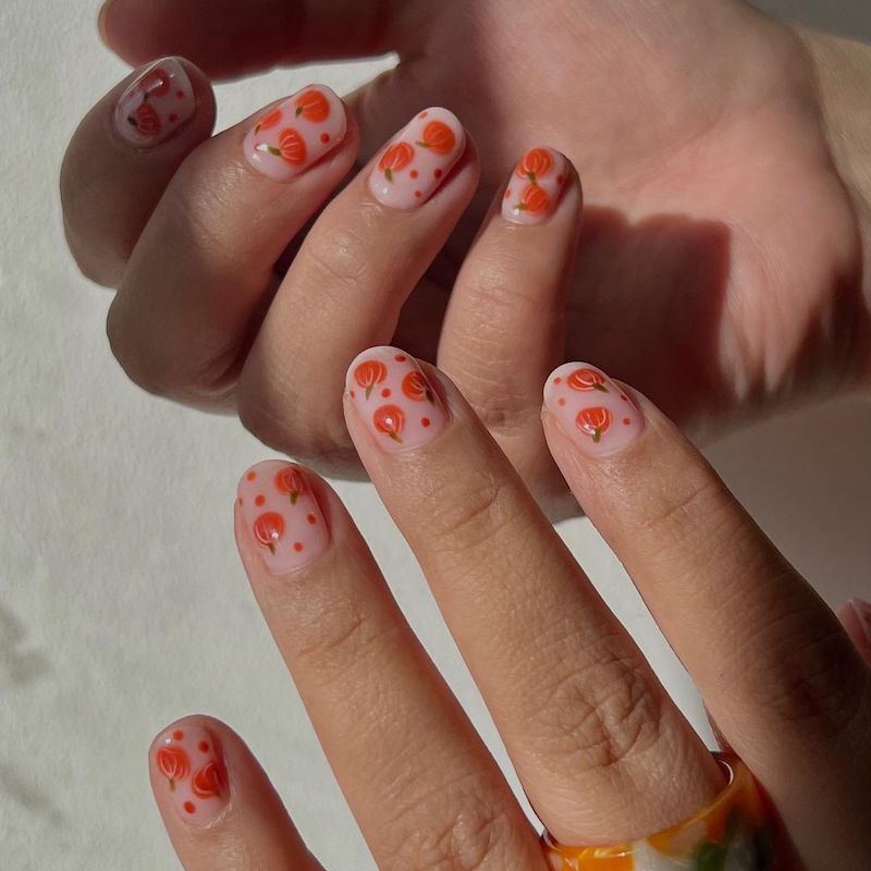 Manicure neutra com pequenos desenhos de abóbora e bolinhas laranja
