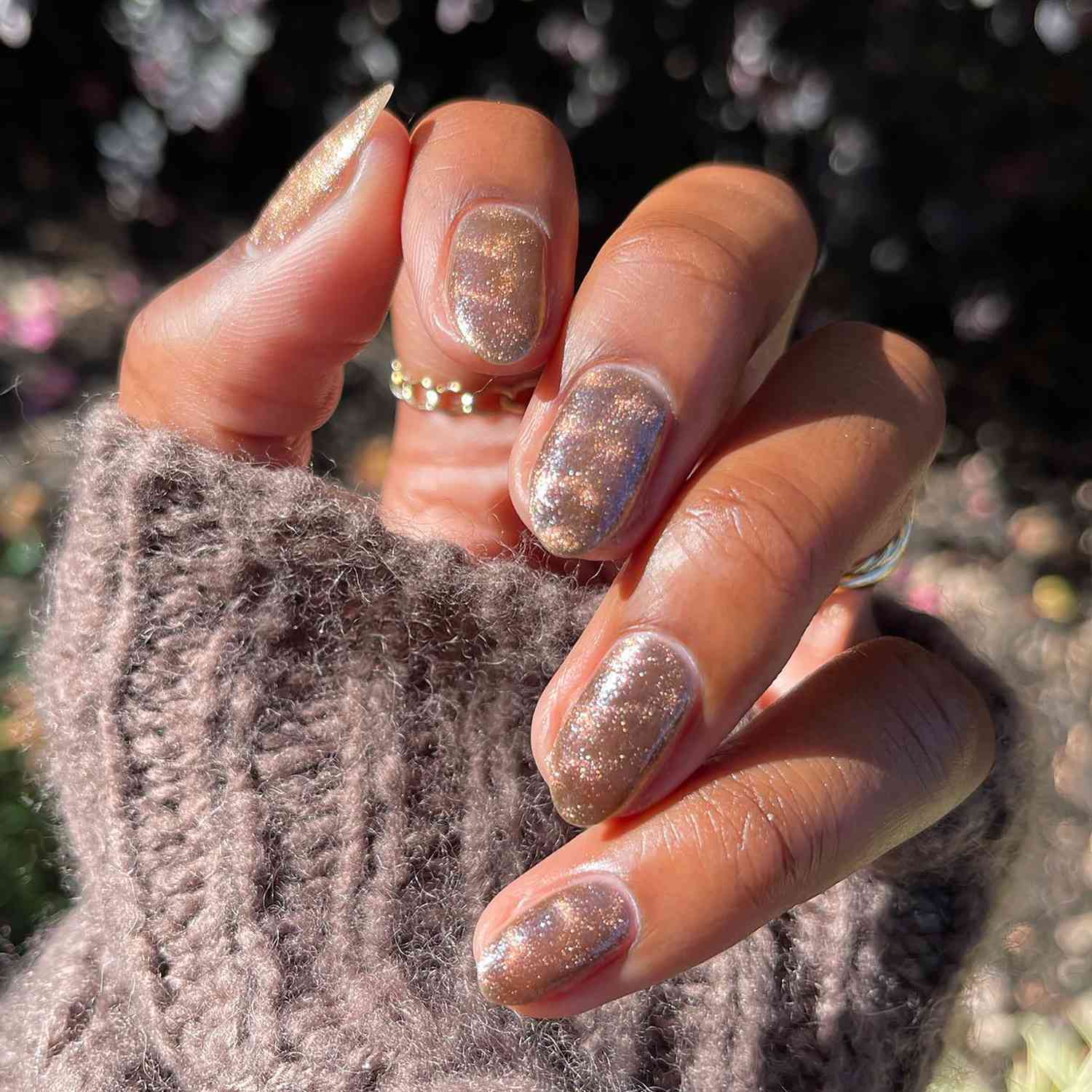 Uma mão em close-up com uma manicure magnética marrom-mel dobrada sobre um suéter grosso
