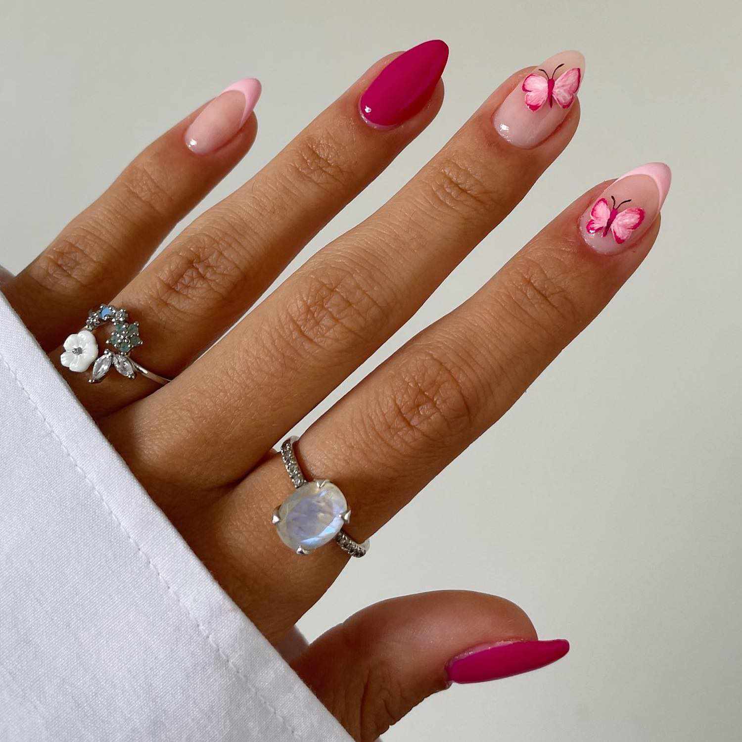 Manicure com unhas rosa quente e lisa e unhas francesas rosa pastel com um design na forma de borboletas rosa