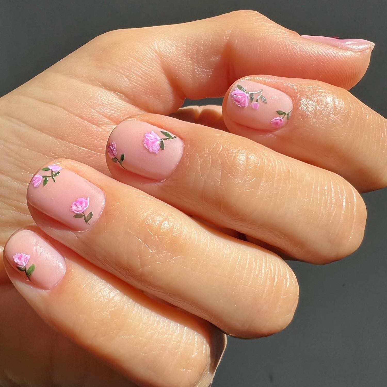 Manicure com uma base nua e rosas rosa desenhadas à mão