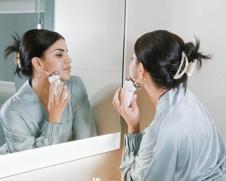 Uma mulher usa uma microcorrente nuface no rosto no espelho