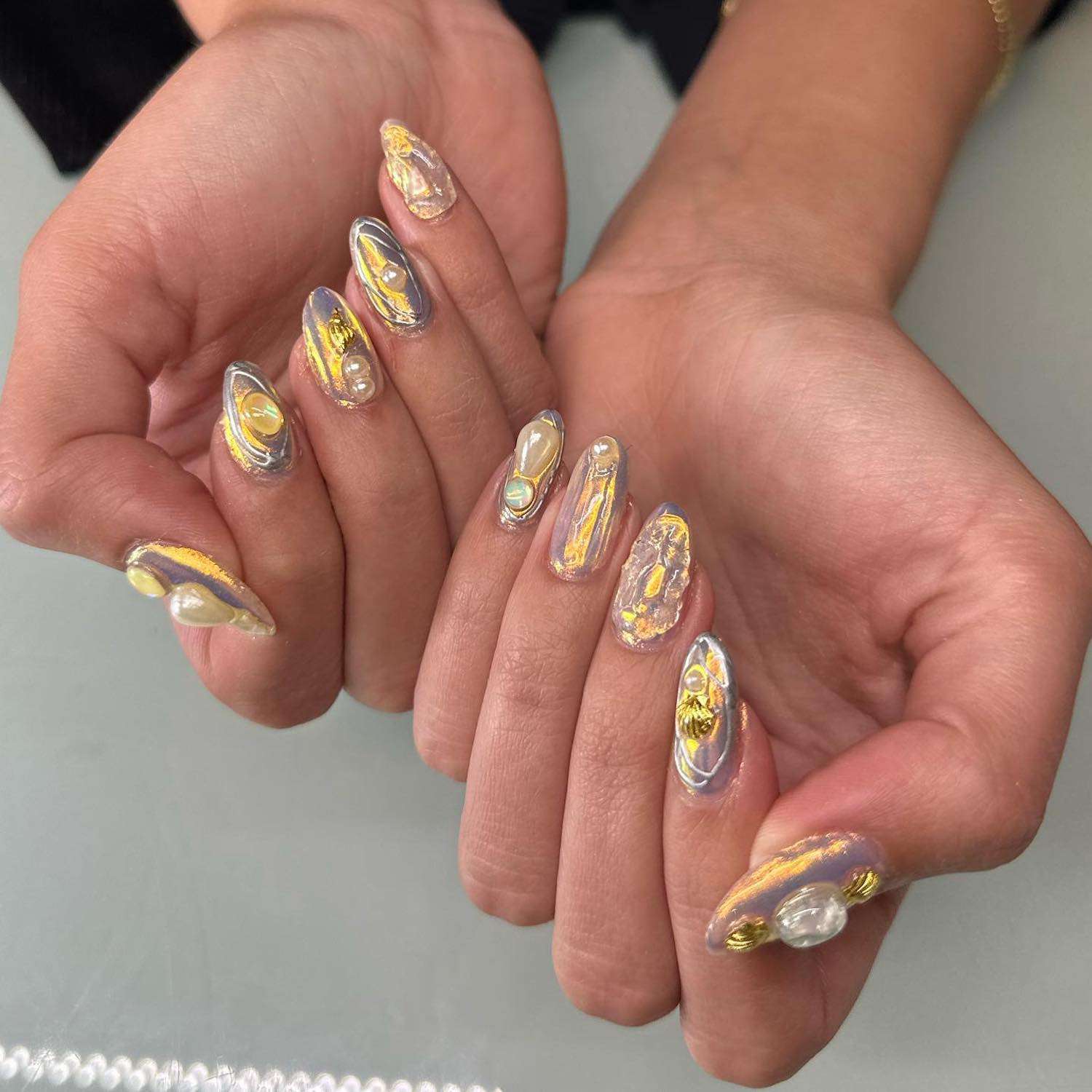 Manicure dourada iridescente inspirada em ostras com detalhes em pérolas