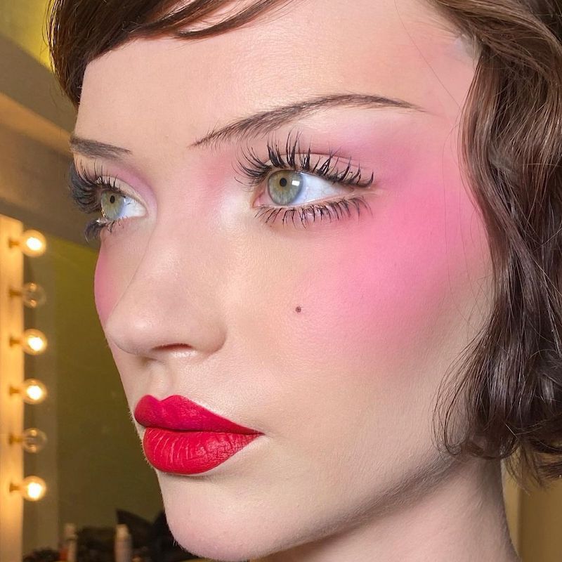 O modelo faz maquiagem no estilo da velha hollywood com blush brilhante, sobrancelhas finas e batom vermelho