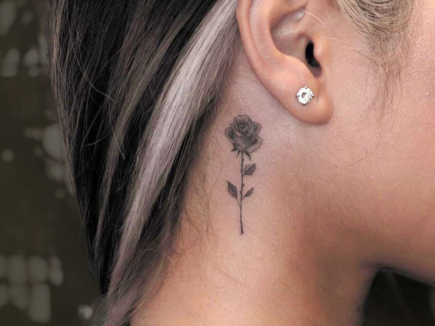 Uma mulher com uma tatuagem de rosa no pescoço atrás da orelha