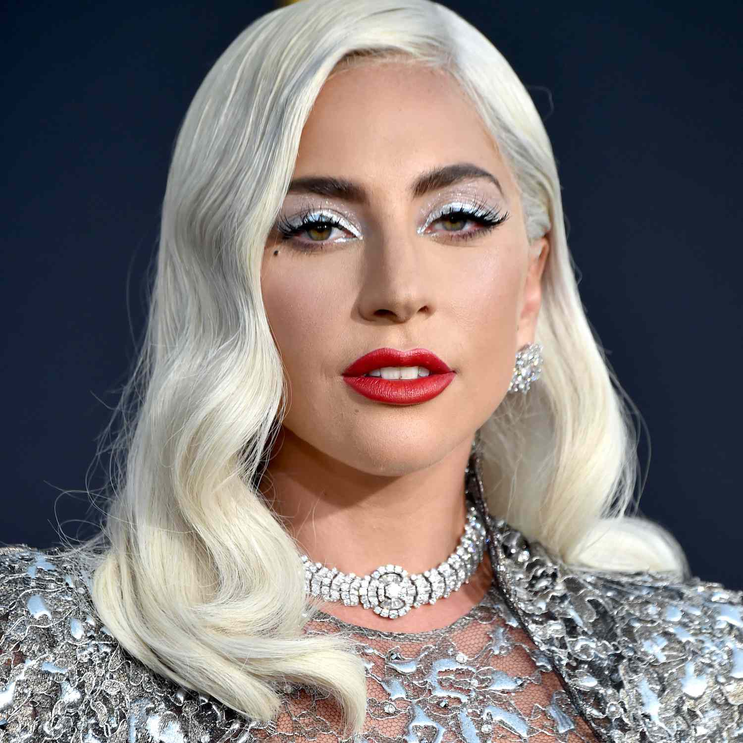 Lady Gaga com sombra branca com glitter prateado, batom vermelho, cosméticos e maquiagem platinada