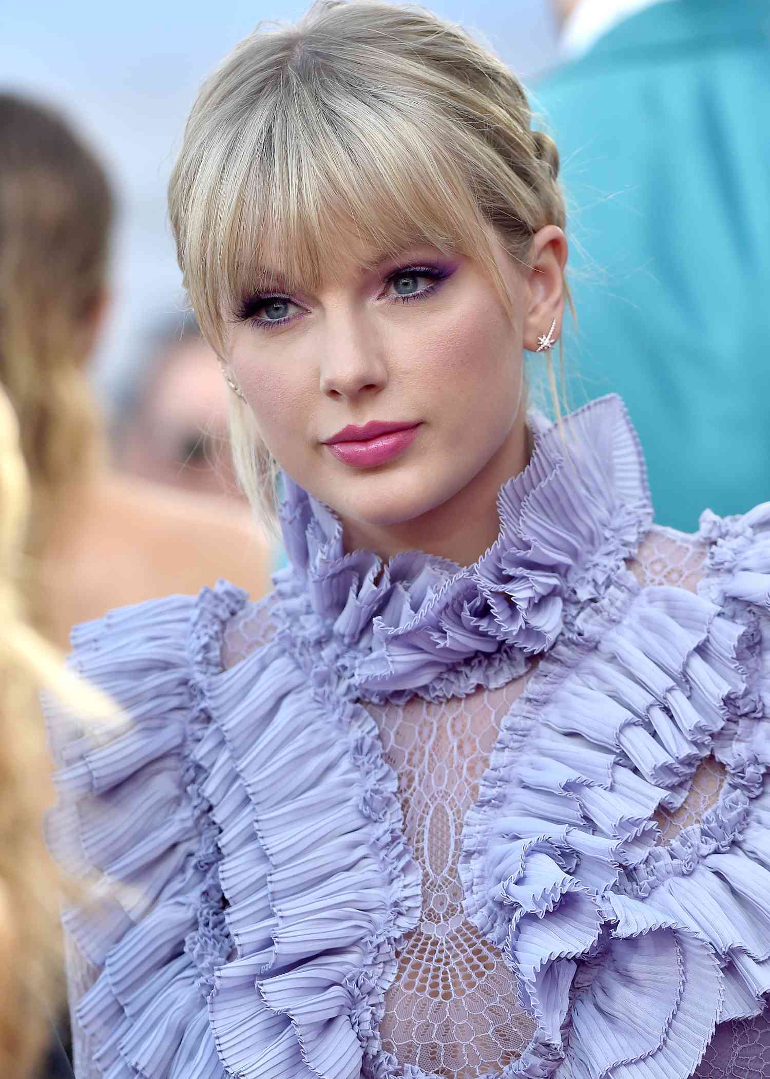 Taylor Swift com maquiagem em tons de rosa e lavanda, em um vestido de lavanda