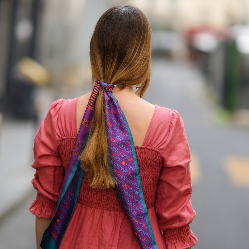 Uma mulher usa uma cauda baixa com um lenço longo com vários coloridos
