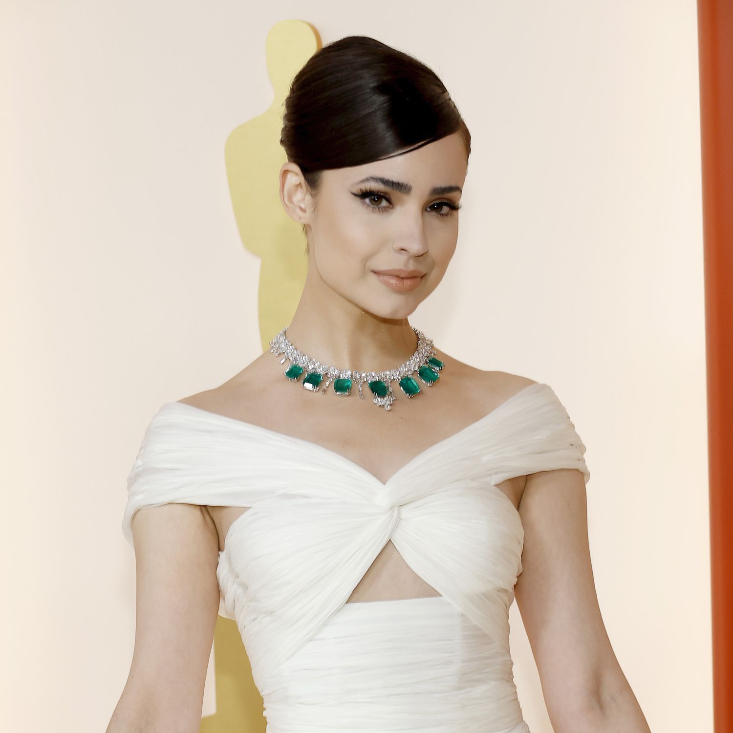 Sofia Carson em vestido branco com colar de esmeraldas