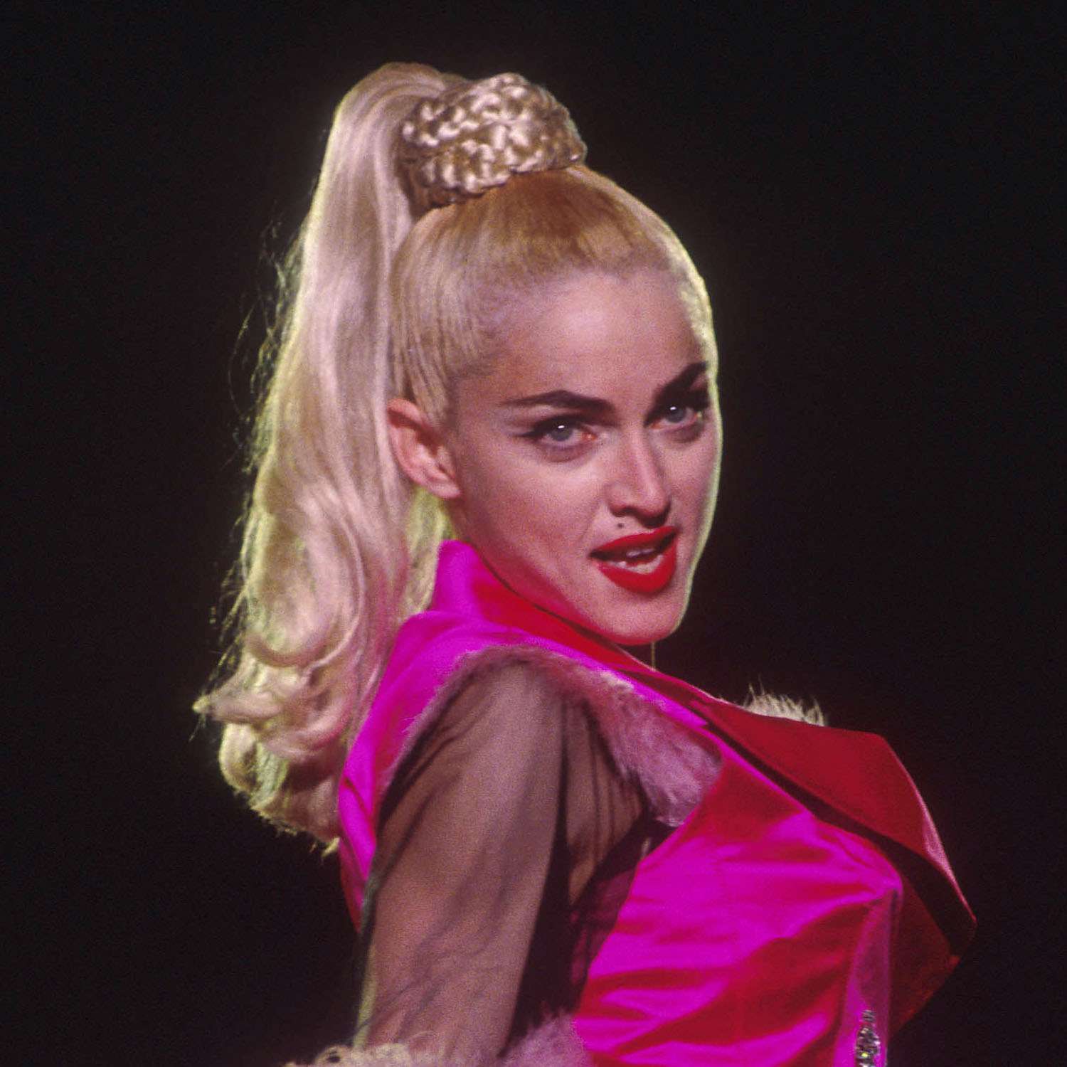 Madonna usa um rabo de cavalo alto platinado com pontas enroladas e base trançada.