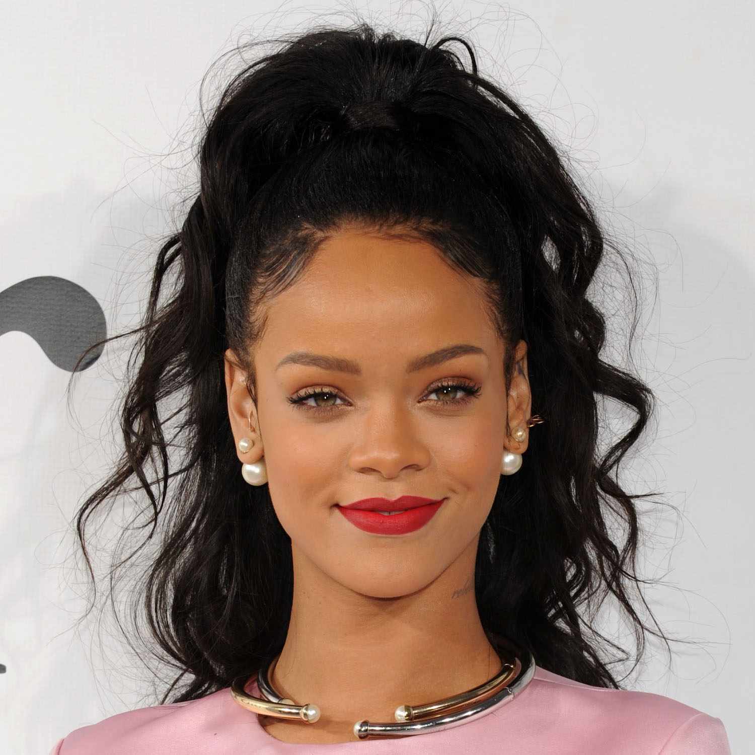 Rihanna com rabo de cavalo alto, brincos de pérola e batom vermelho.