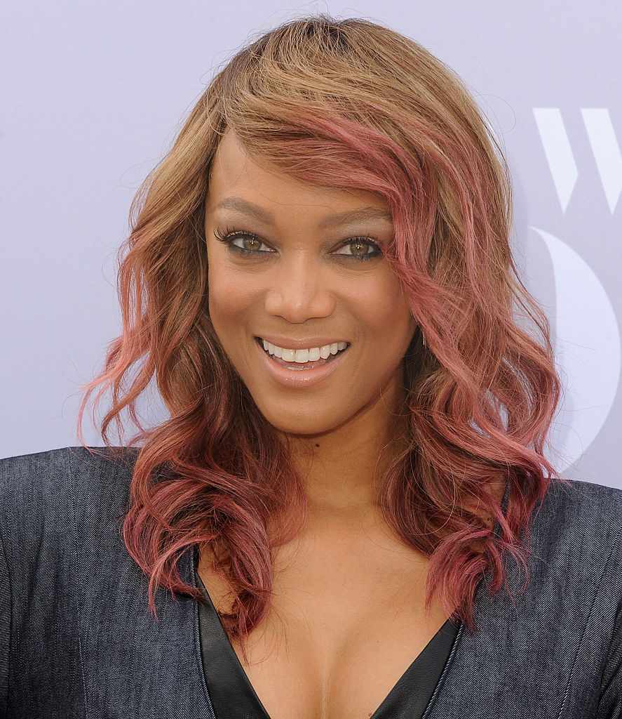 Tyra Banks com cabelos ondulados de comprimento médio com brilho rosa