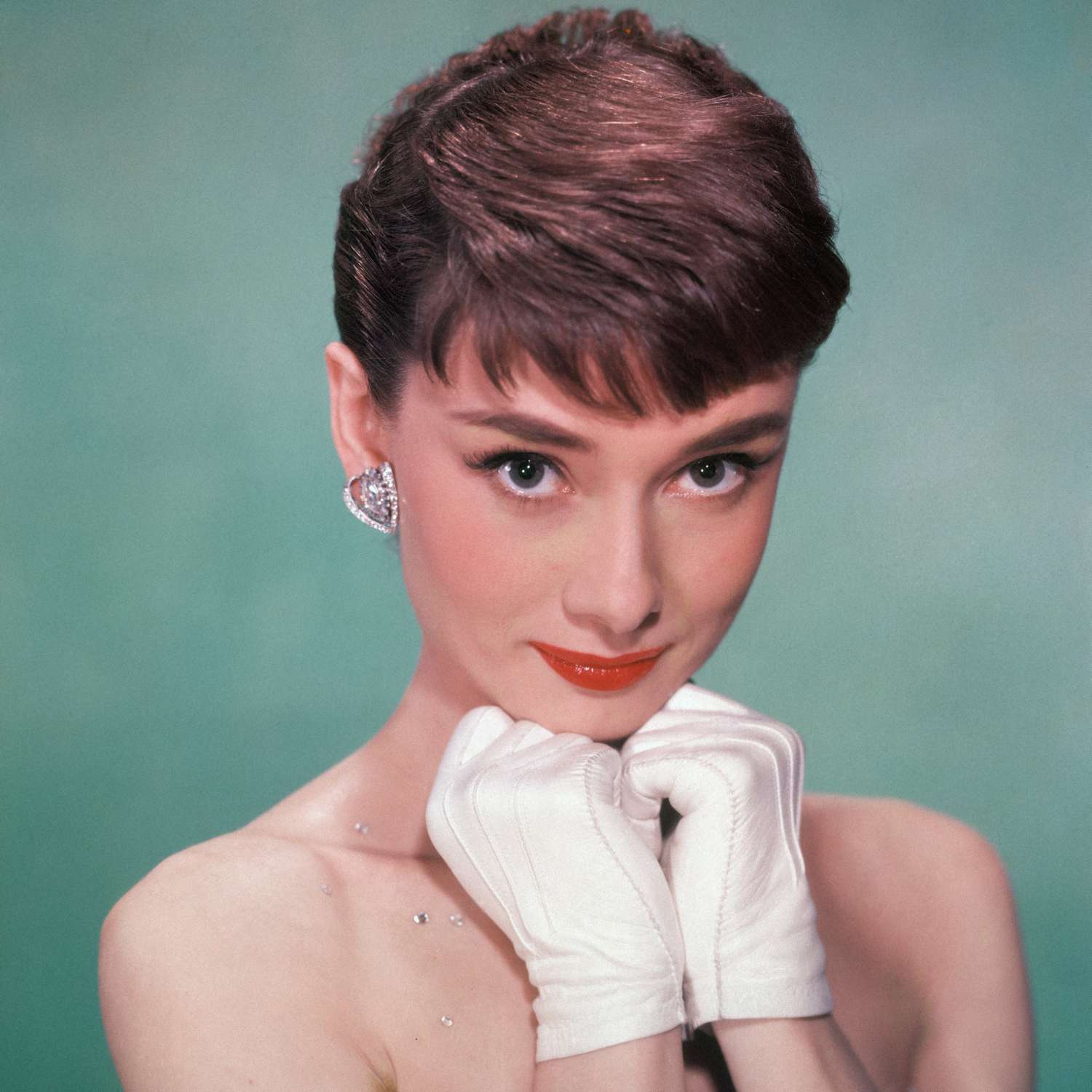 Audrey Hepburn em um vestido sem tiras e com as mãos brancas nas luvas infantis no queixo, o início de 1950