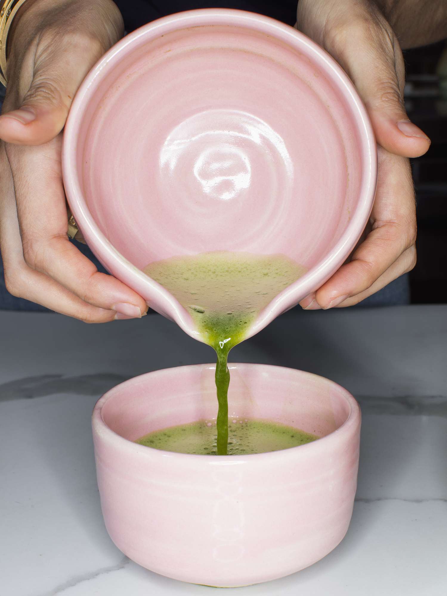 Mãos derramando chá verde em uma caneca rosa