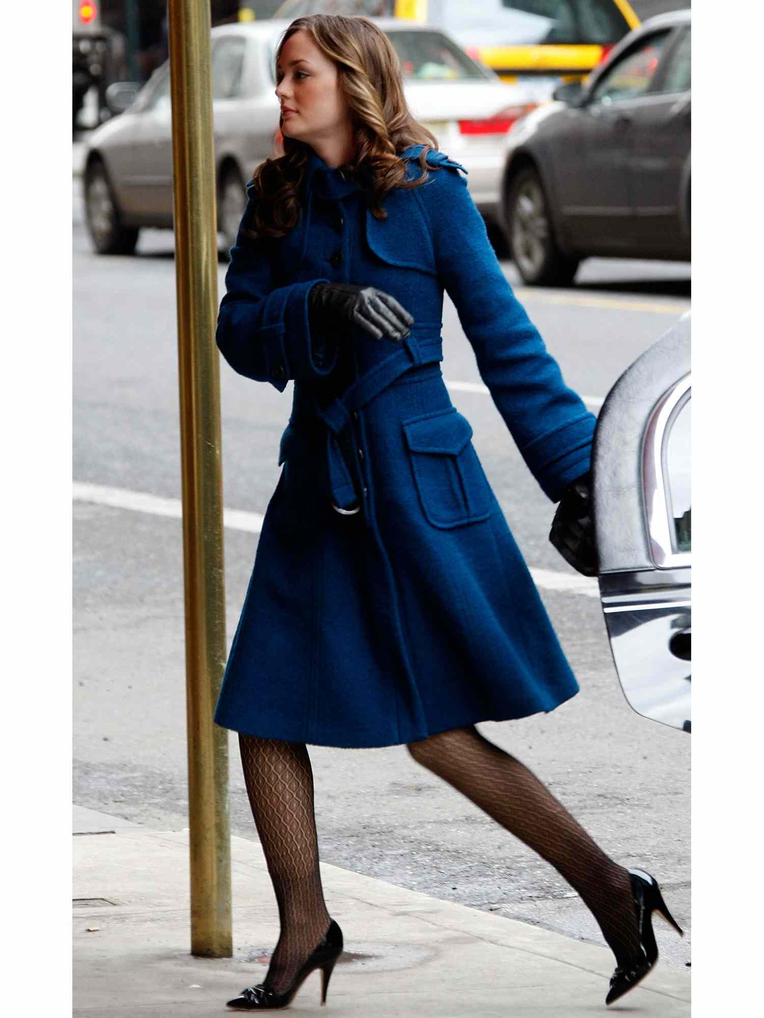 Leighton Meszer no papel de Blair Waldorf em um longo casaco azul escuro com sapatos de salto alto preto e meia-calça com padrões