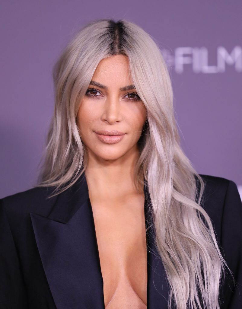 Kim Kardashian com longos cabelos grisalhos ondulados com raízes escuras