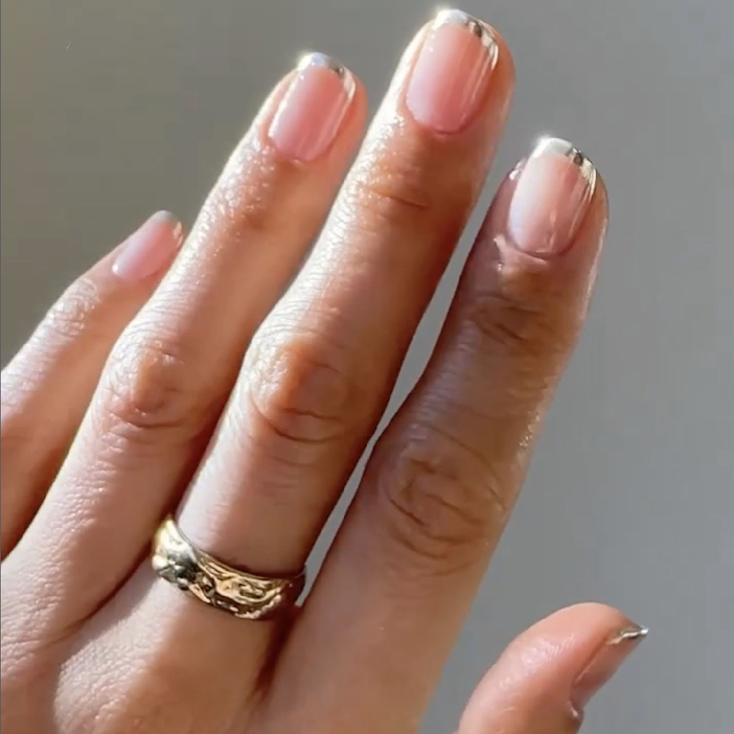 Plano próximo de uma manicure francesa cromo prateada com um anel no dedo médio