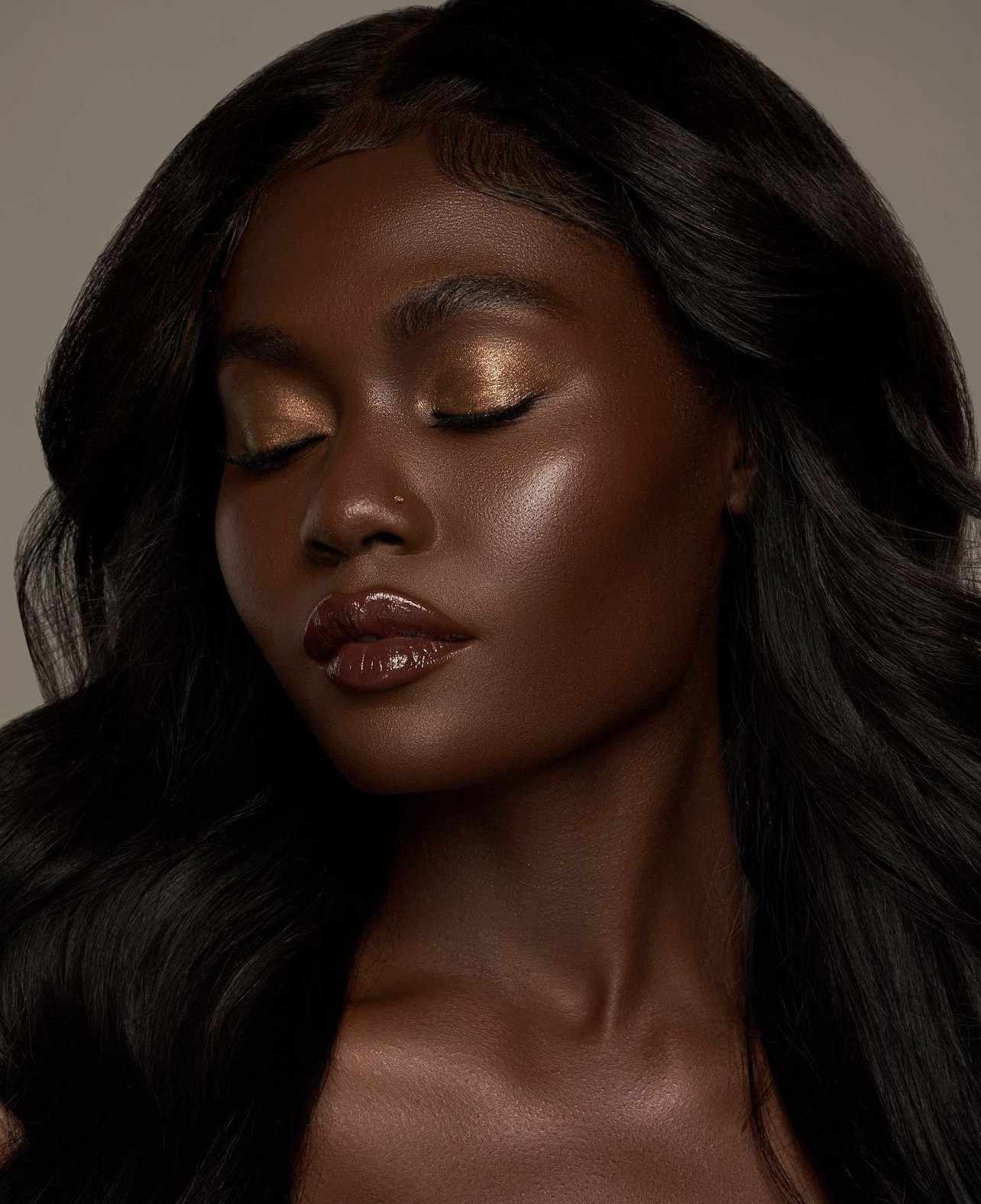 A modelo de pele escura usa sombra cobre cintilante e batom rico e brilhante.