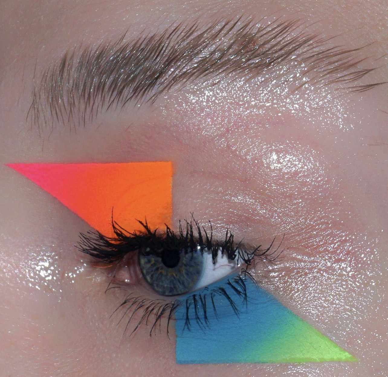 Sombras gráficas neon em tons de néon laranja, rosa, azul e verde na forma de um triângulo agudo acima e sob o olho foram aplicados às pálpebras