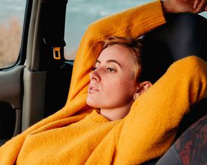 Uma mulher de suéter laranja se inclina para trás no carro