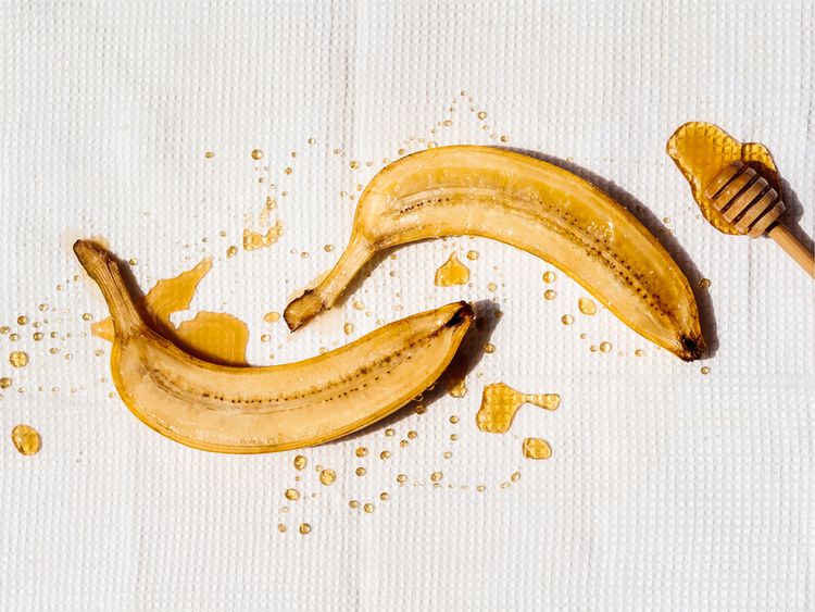 Banana cortada ao meio, regada com mel, em um fundo branco
