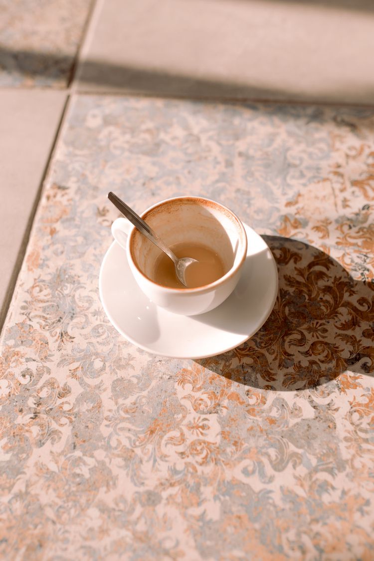 Xícara quase vazia de café em um rack de azulejos com uma colher pequena em uma xícara
