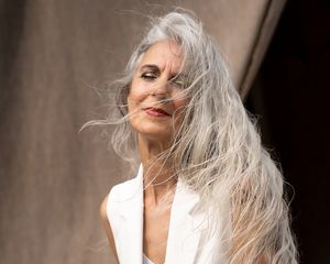 Uma mulher com longos cabelos brancos ao vento, posando no fundo do fundo bege