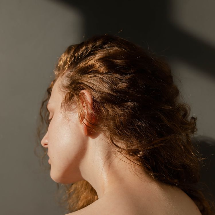 O fechament o-up dos cabelos loiros ondulados de uma mulher está para trás, seu pescoço é visível