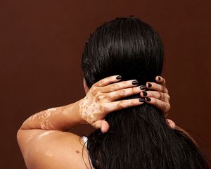 Costas da mulher isoladas em fundo marrom de estúdio, mãos no cabelo