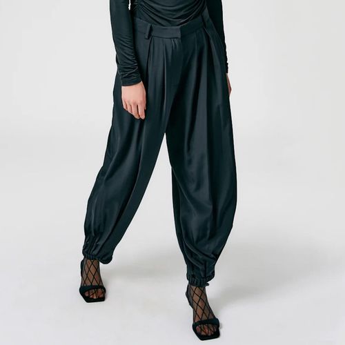A modelo usa calça balão plissada de seda Tibi Eco em preto combinada com sapatos de bico quadrado e blusa preta de manga comprida
