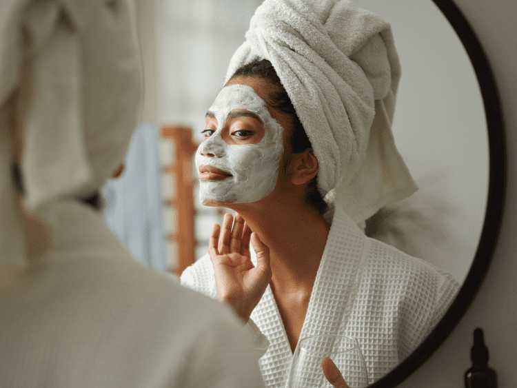 Um close de uma mulher que está olhando em um espelho com uma máscara no rosto durante um spa