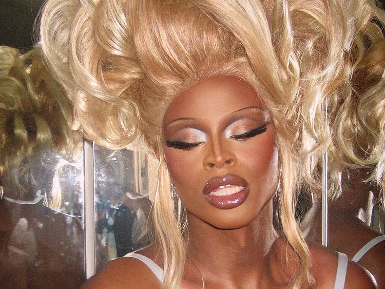 Close da drag queen Simon com sobrancelhas finas e maquiagem dos anos 90.
