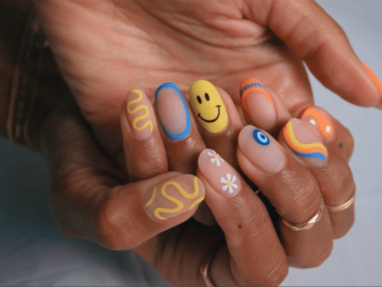 Close de uma mão com unhas foscas e designs de emoji e til