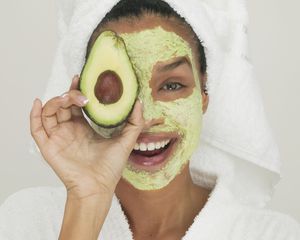 Retrato de uma jovem usando uma máscara facial segurando uma fatia de abacate