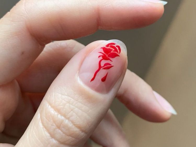 O grande plano do polegar com sotaque na forma de uma rosa vermelha