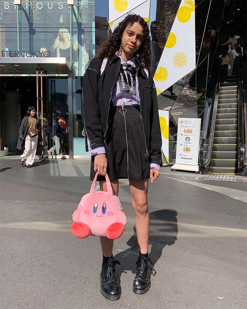 Uma mulher de saia preta e uma bolsa na forma de um Pokmon