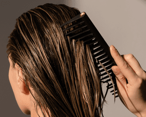 A mulher passa um pente através de cabelos molhados