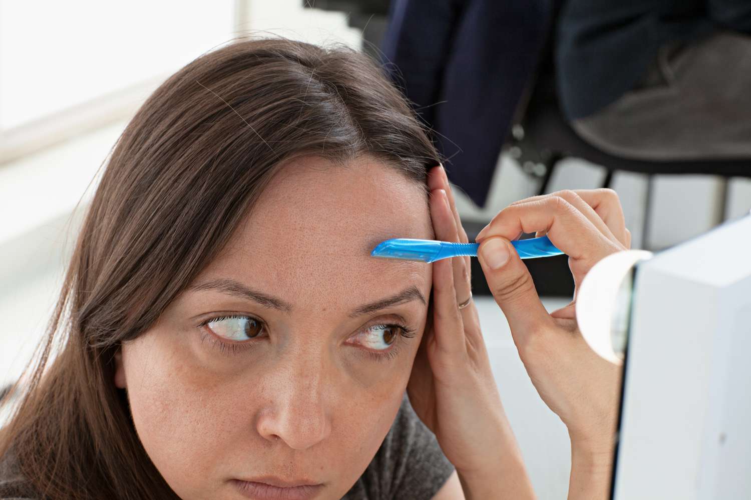 Mulher usando a ferramenta de dermaplanagem esfoliante Schick Hydro Silk Touch-Up na testa em frente ao espelho