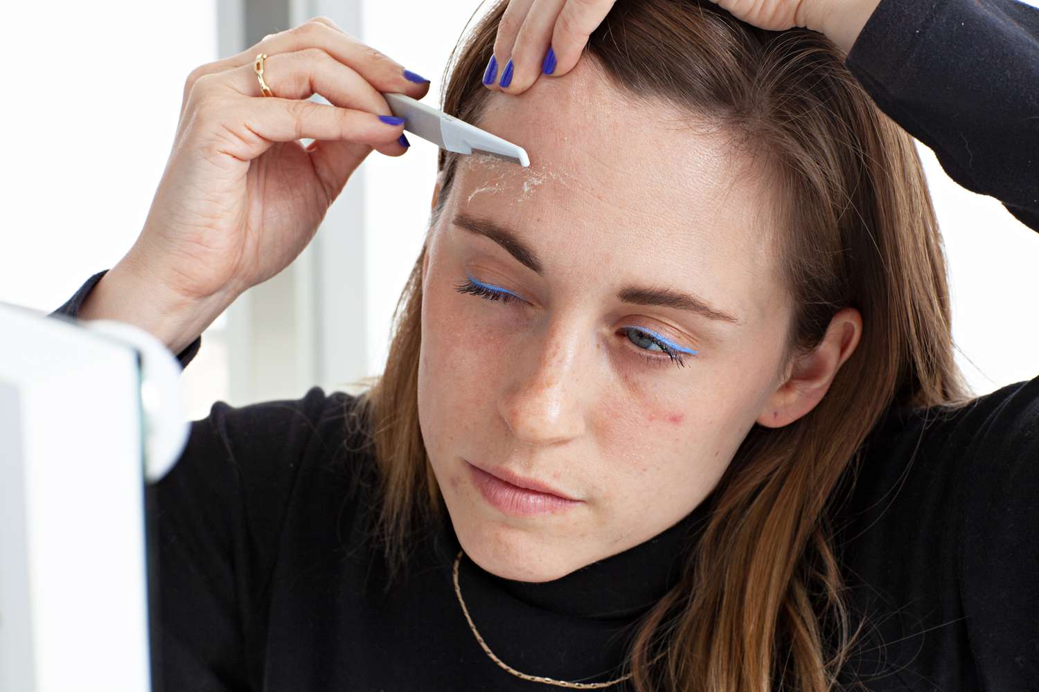 Mulher usando a ferramenta Stacked Skincare Dermaplaning na testa para esfoliar o rosto