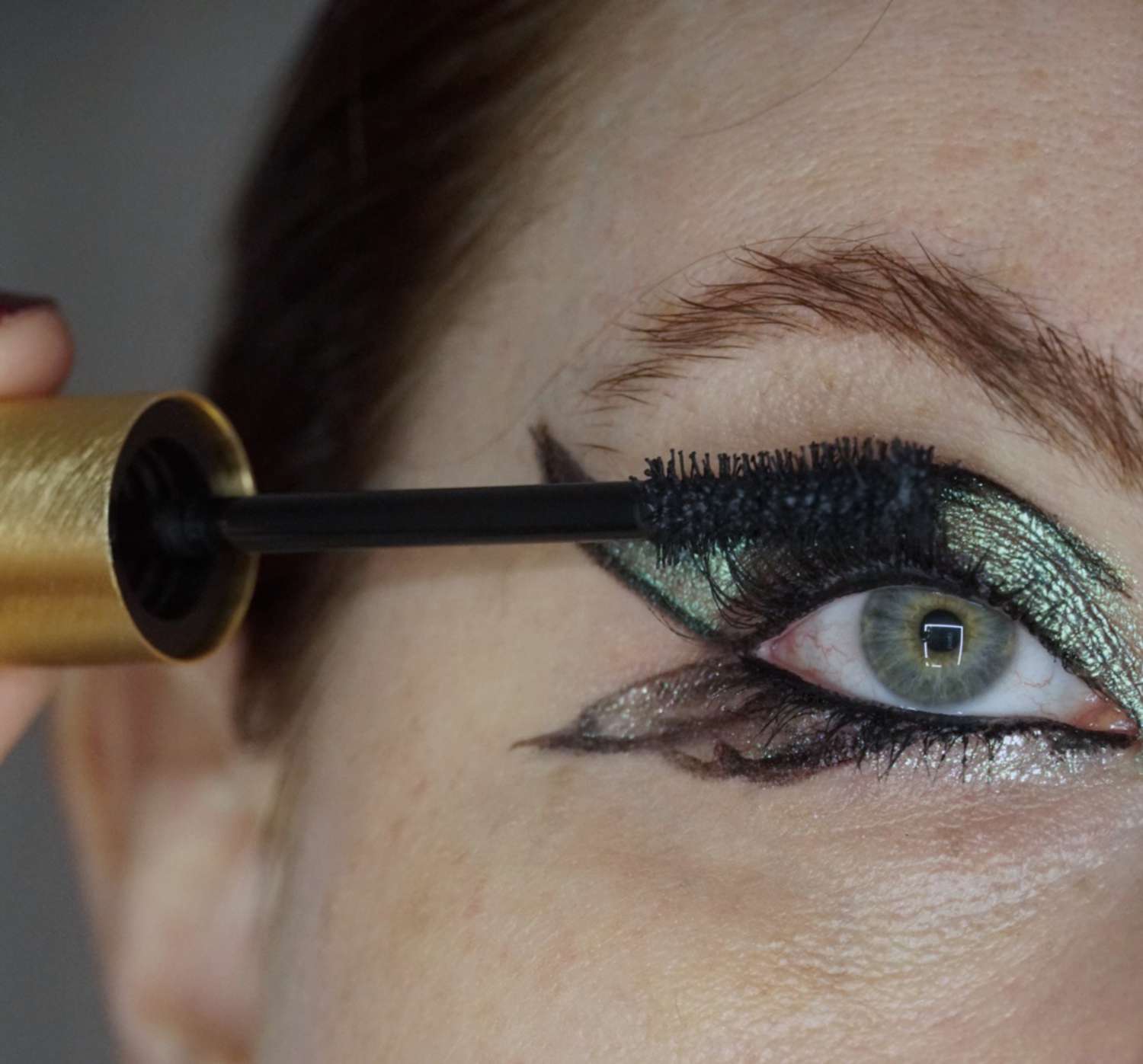 Uma mulher próxima que aplica rímel de cílios para maquiagem completa com sombras e um delineador em forma de borboleta